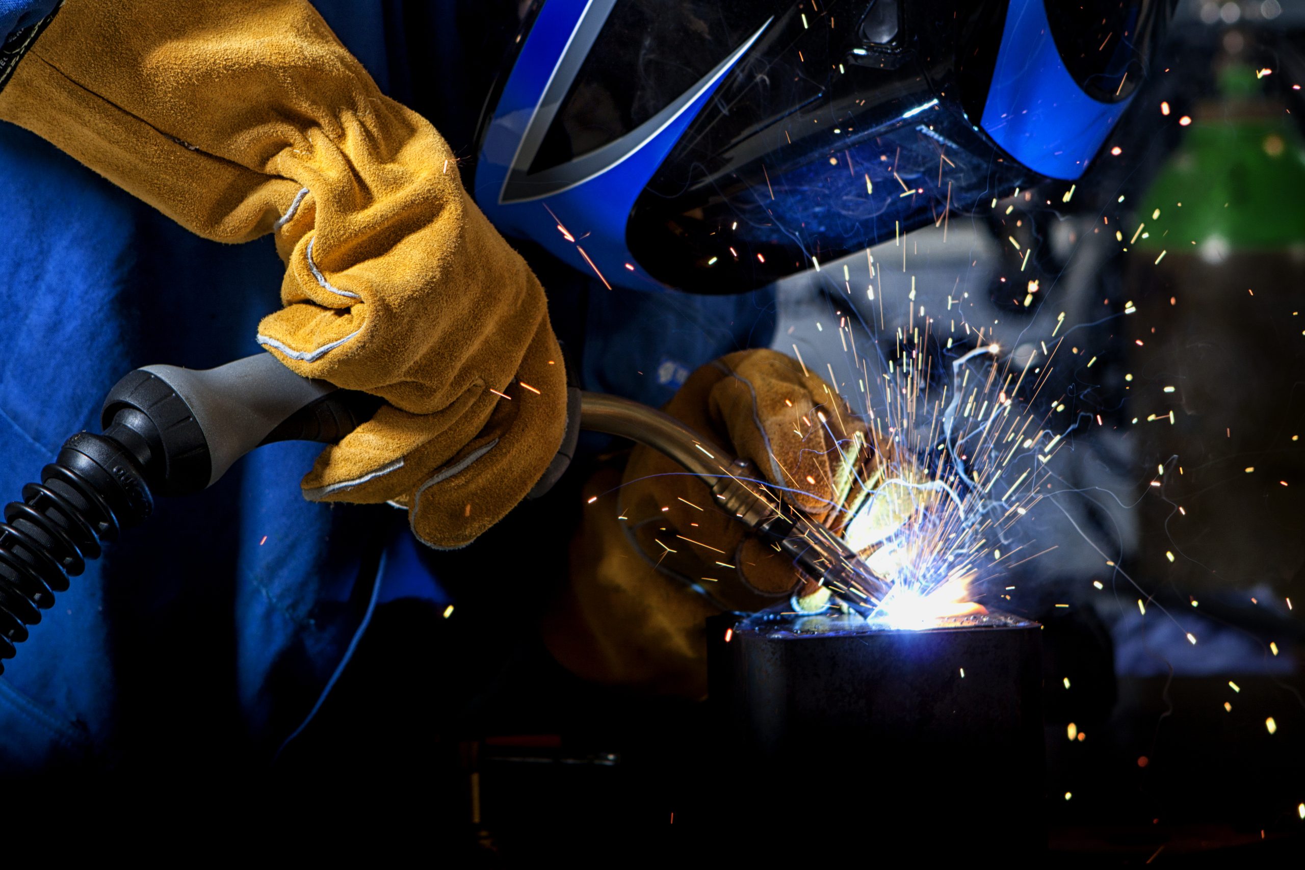 Welder wearing gloves and mask with welding sparks.